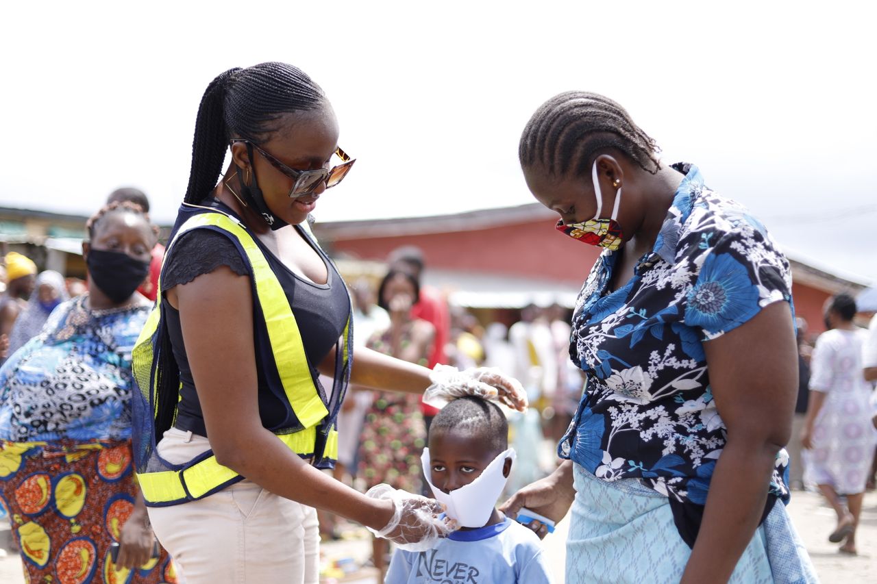 Women assisting a child with face mask in a community street setting.